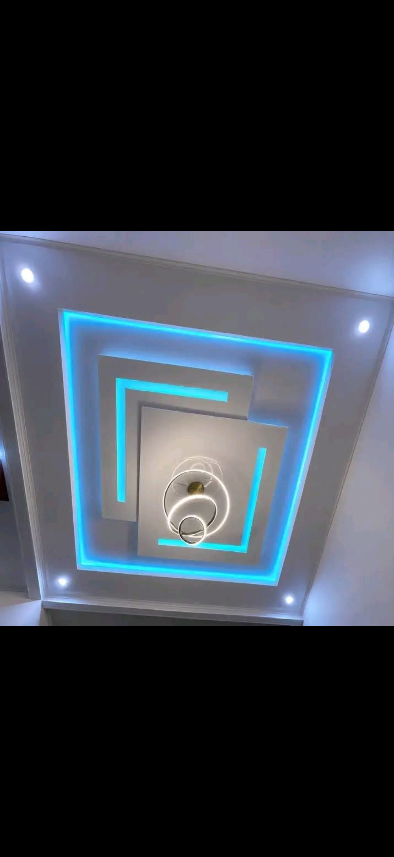 Drywall ceiling formed by nested spiraling squares outlined in blue LED lighting with a ring chandelier