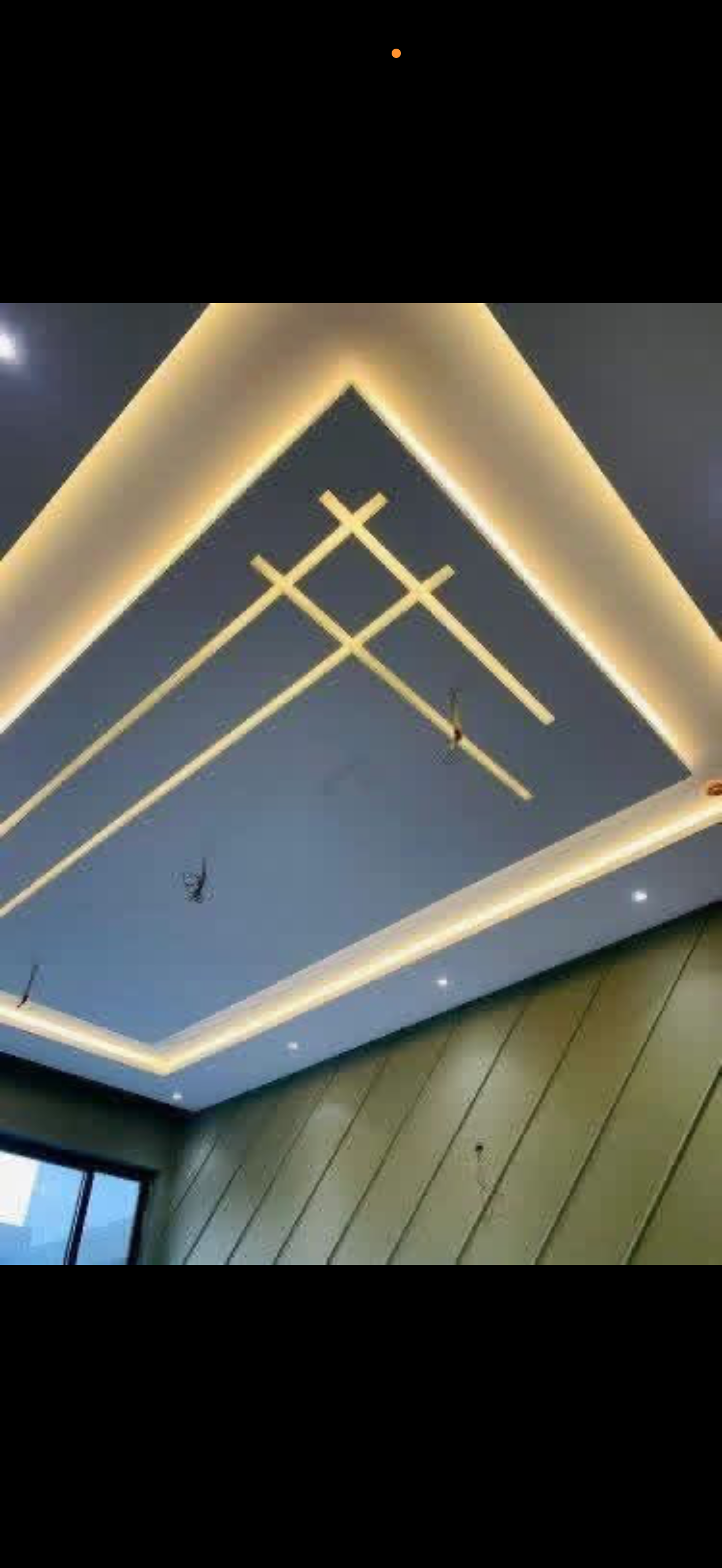 Gray ceiling with a chevron geometric design formed by warm LED strip lines beside a wood-paneled accent wall