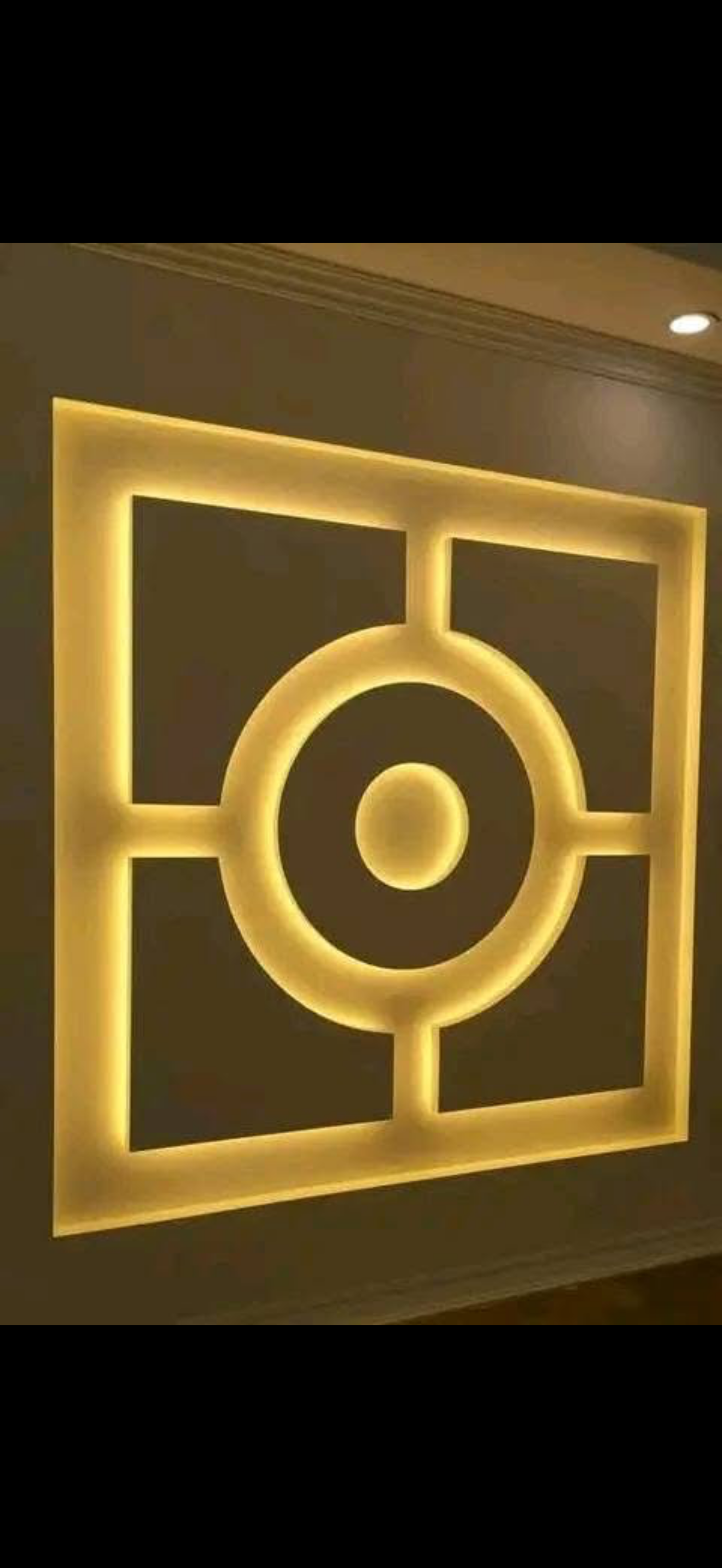 Square drywall wall panel with a concentric circle medallion motif backlit by warm gold LED cove lighting