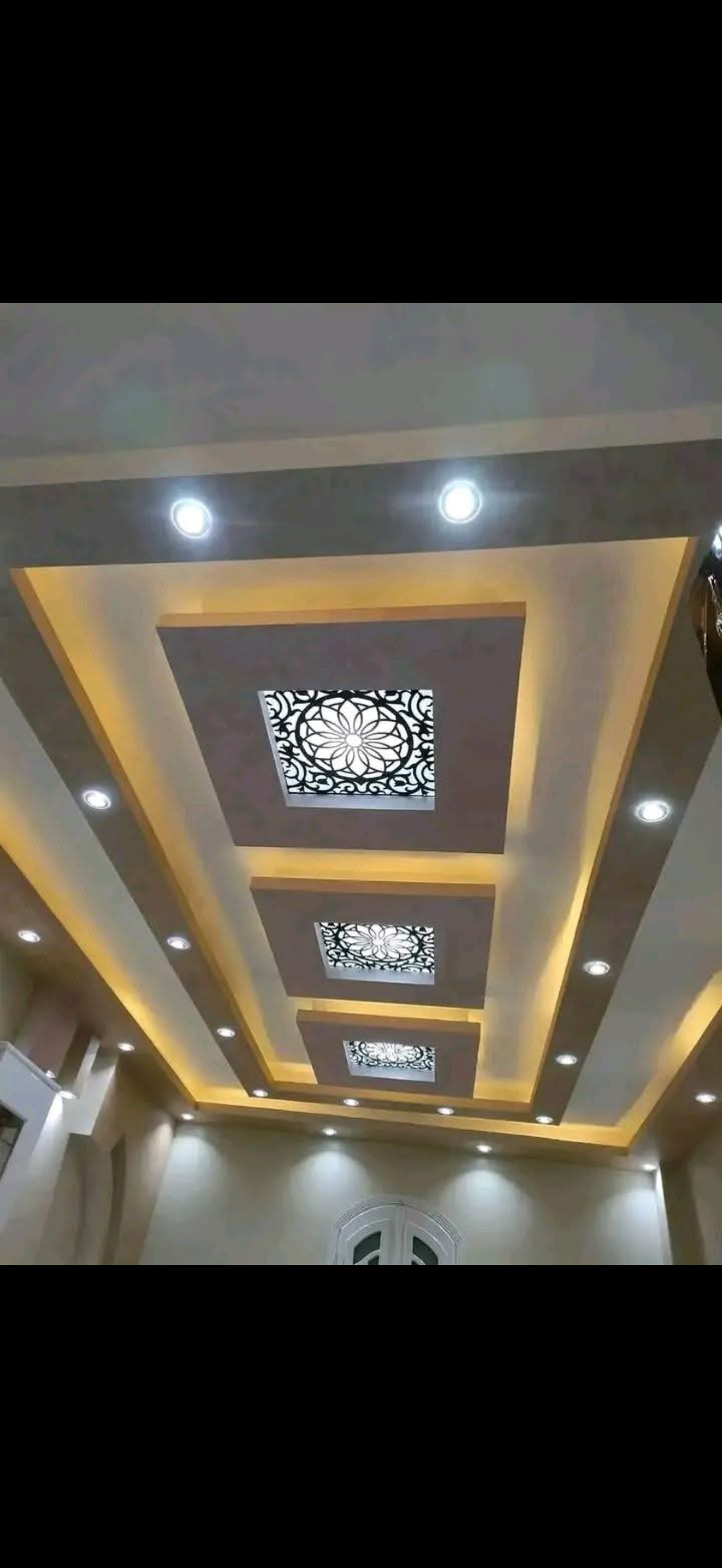 Layered stepped drywall tray ceiling with laser-cut floral mandala panels, warm cove lighting and recessed spotlights