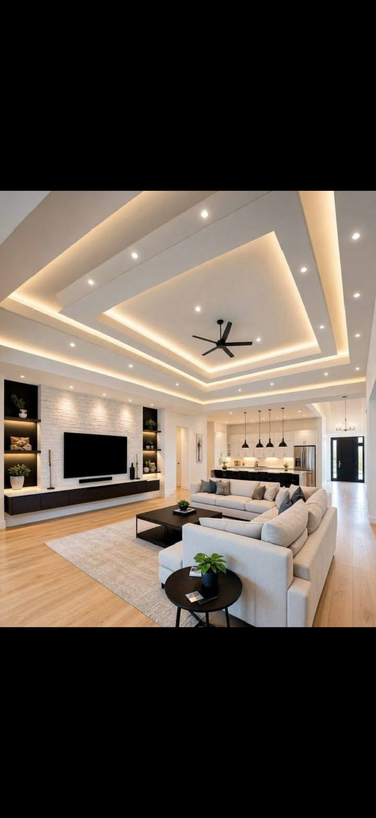 Large open-plan living room with a tiered drywall tray ceiling, warm cove lighting, recessed spots and a built-in media wall