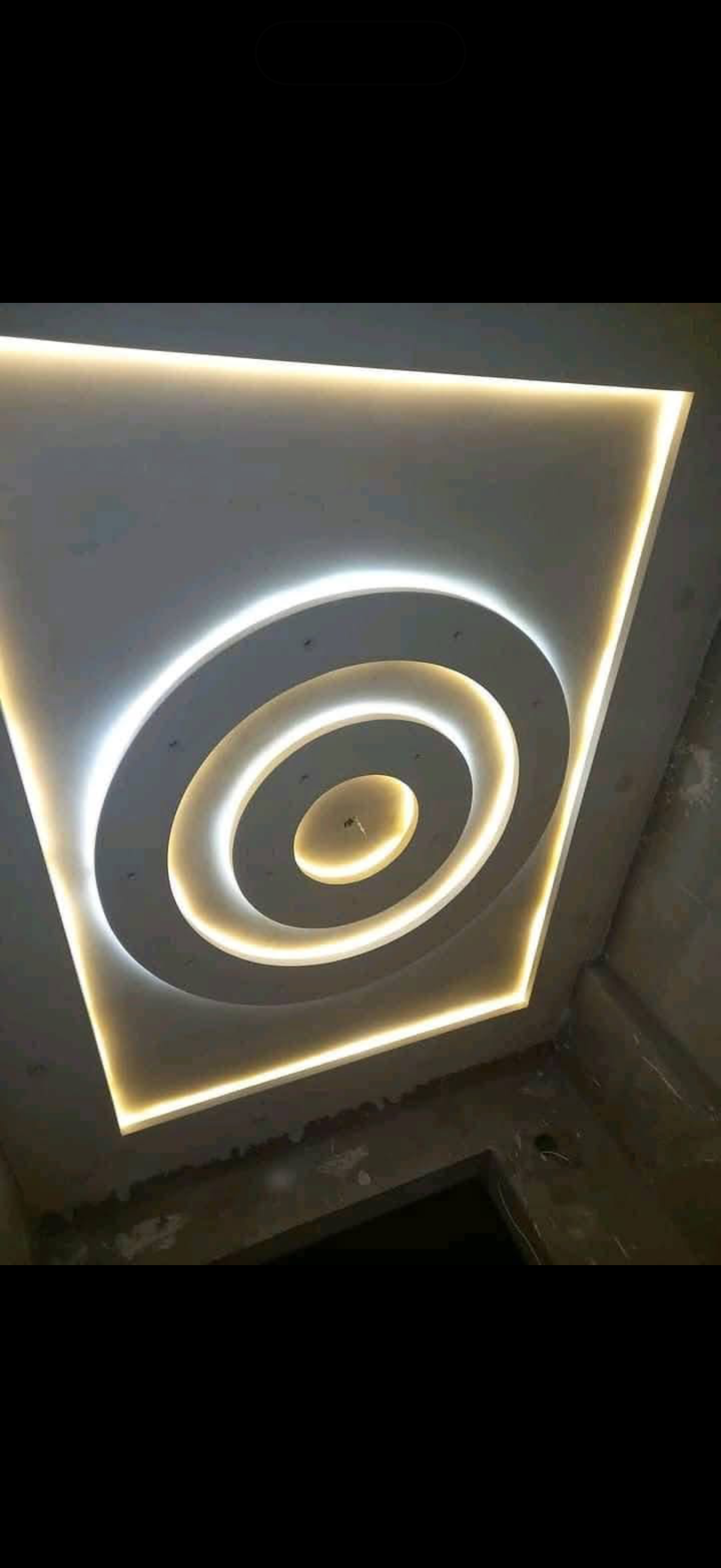 Drywall ceiling with concentric oval recessed rings lit by warm LED cove lighting