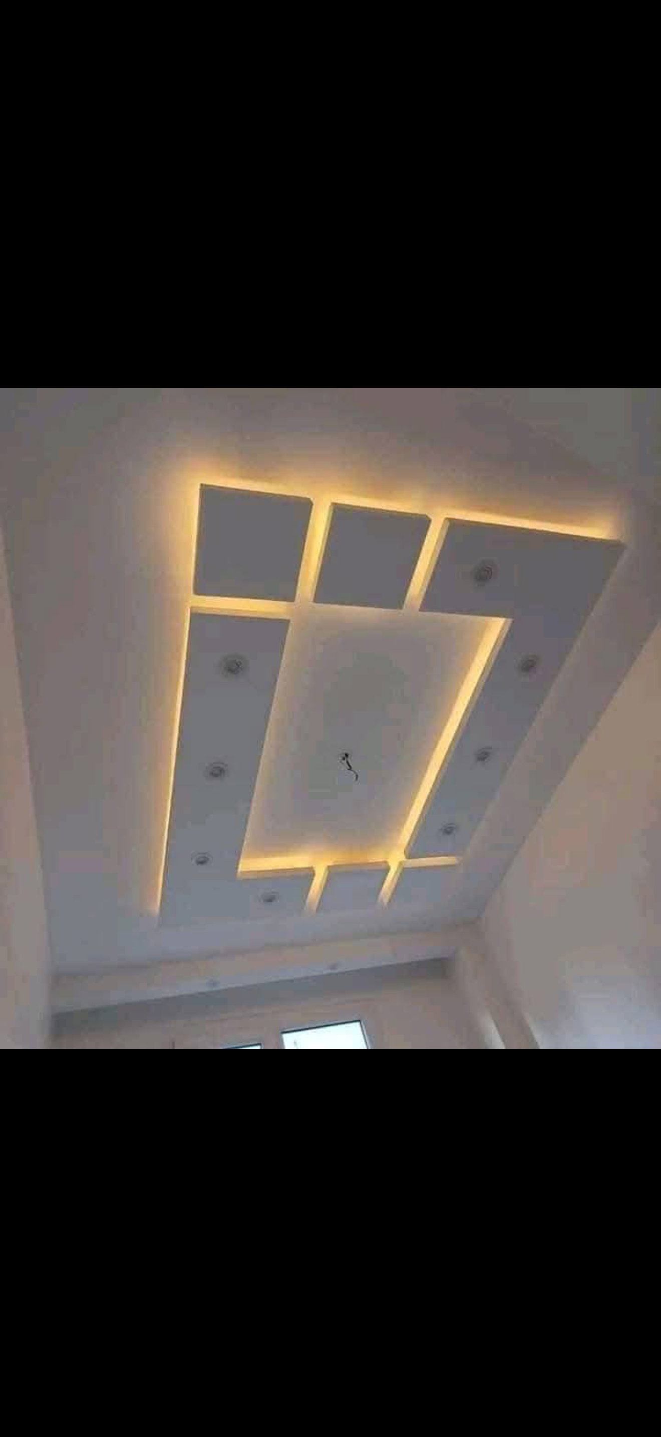 White drywall ceiling composed of offset rectangular panels separated by warm LED backlit gaps and recessed spotlights