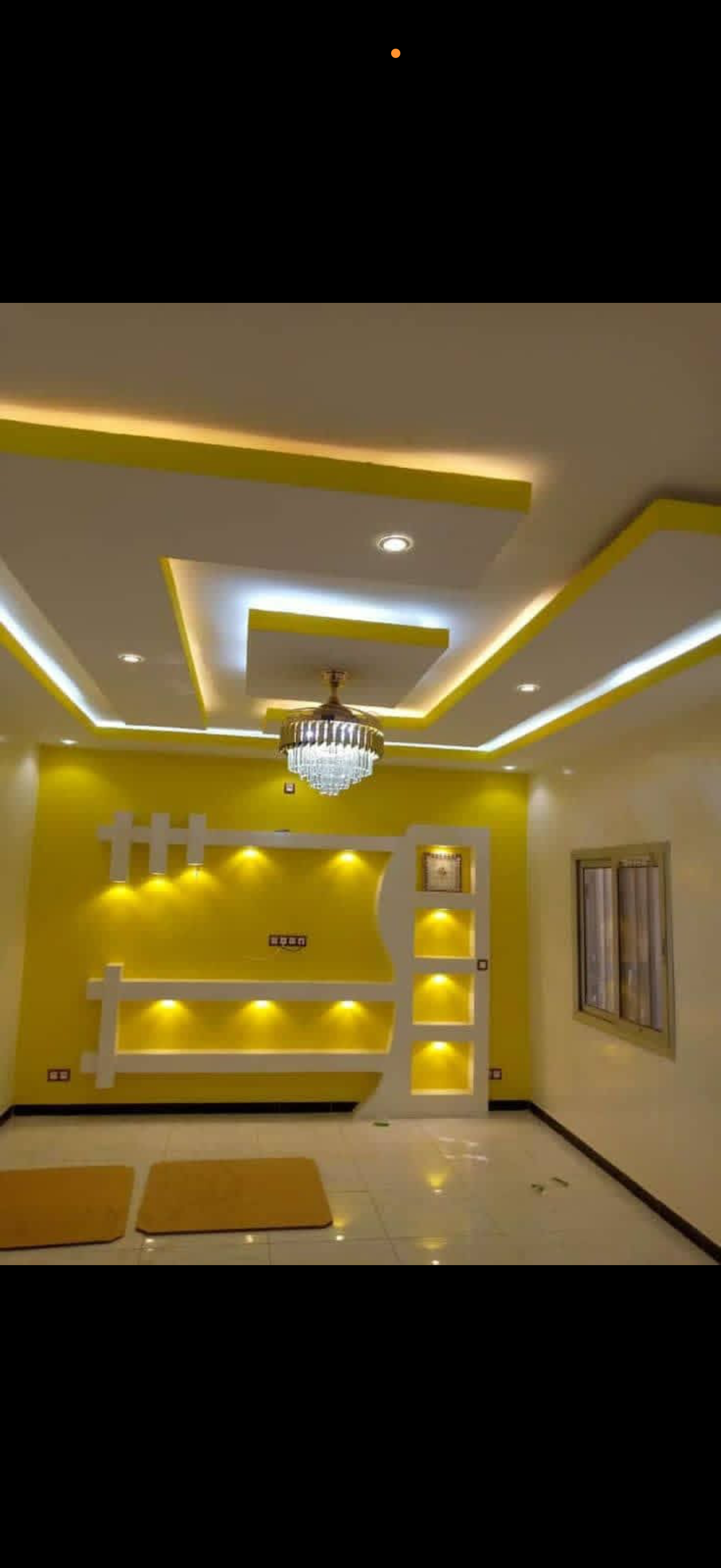 Living room with a multi-tier tray ceiling, chandelier and a yellow accent feature wall with lit display niches and shelving